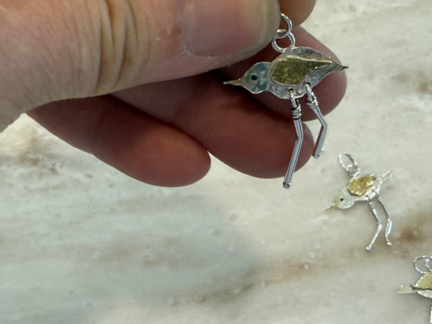 Hand holding a silver bird pendant against a marble background