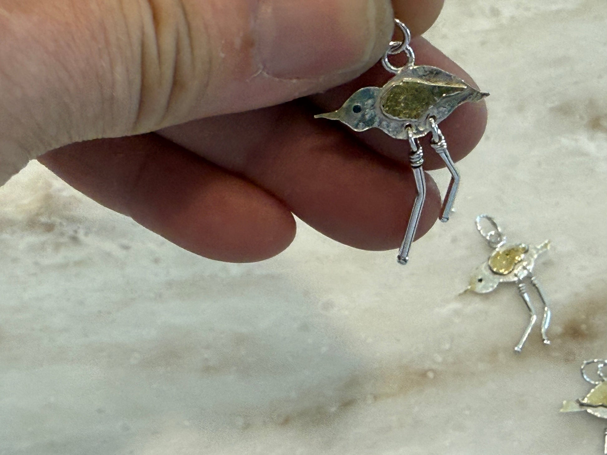 Hand holding a silver bird pendant against a marble background