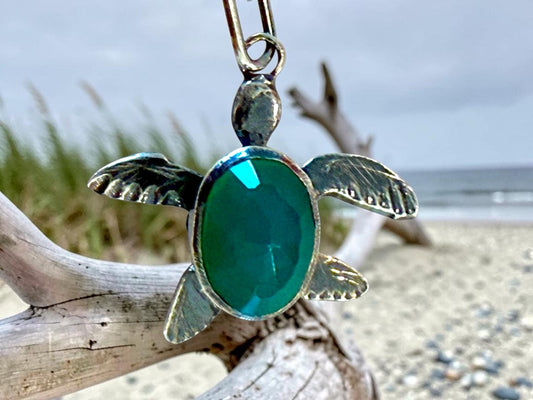 Green onyx turtle charm hanging on driftwood at the beach