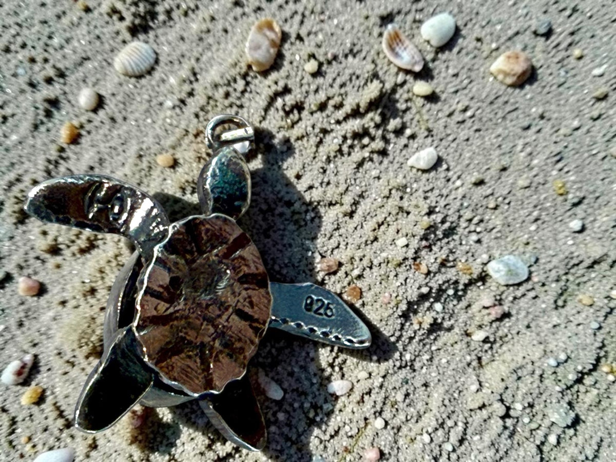 Underside of the green onyx turtle charm on the sand, showing the articulated flippers