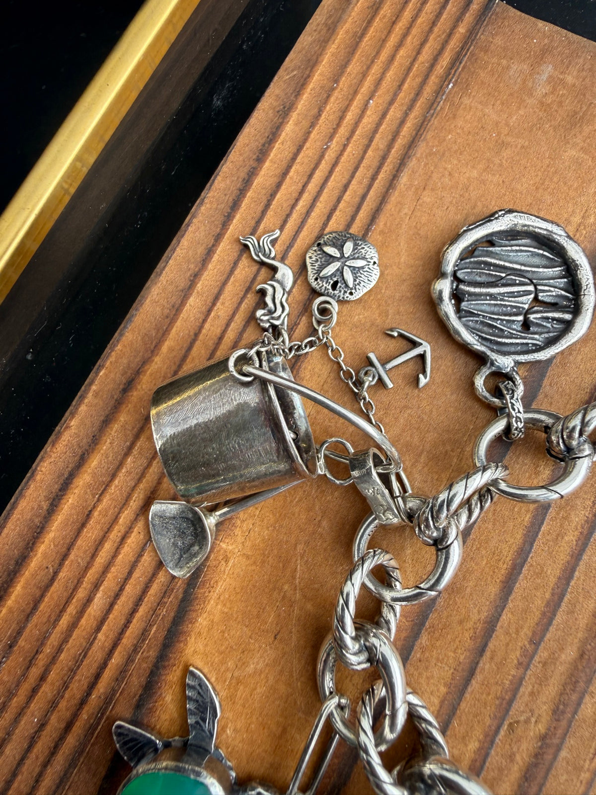 Sand castle bucket charm with shovel, mermaid, sand dollar, and anchor, shown on a charm bracelet