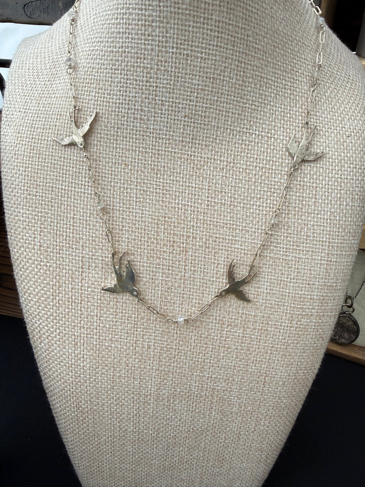 Sterling silver swallow necklace with lab-grown diamond eyes and moonstone beads, shown on a bust