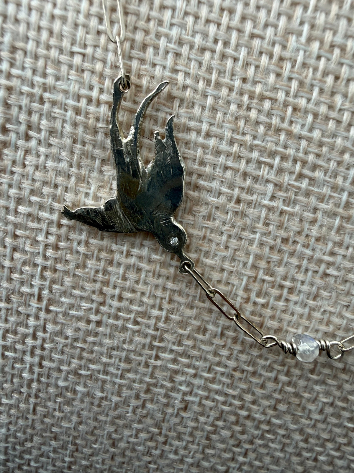 Swallow detail — sterling silver swallow with a lab-grown diamond eye and a moonstone bead on the chain